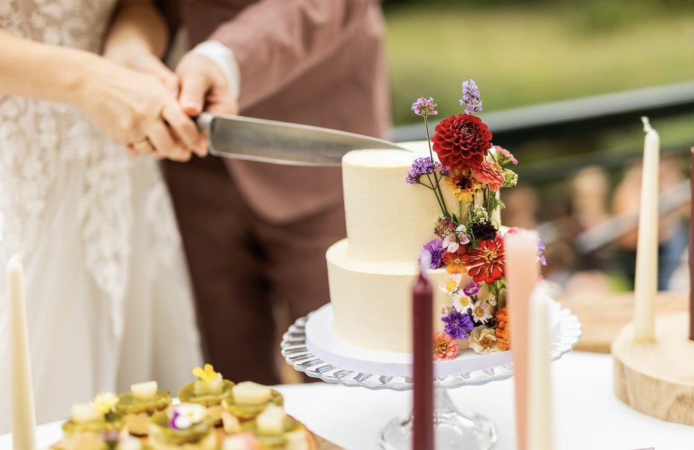 Tweelaagse bruidstaart met kleurrijke bloemen op een glazen taartstandaard