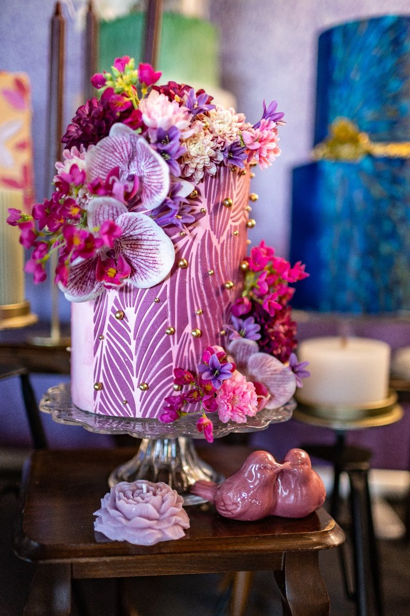 Hoge paarse bruidstaart met bloemen en gouden parels