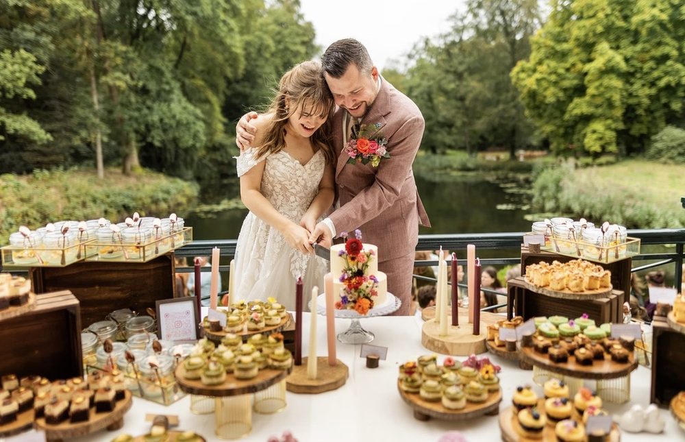 Bruidspaar snijdt de bruidstaart aan tussen een rijk gevulde sweettable